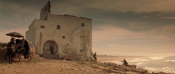 Movie still from “Malena” (2000), directed by Giuseppe Tornatore – Two people are standing on the beach near a building; Extreme Wide shot, Low angle