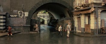 Movie still from “Malena” (2000), directed by Giuseppe Tornatore – A group of men walking down a wet street; Wide shot, High angle