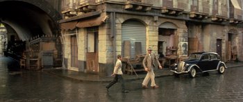 Movie still from “Malena” (2000), directed by Giuseppe Tornatore – Two men walking down the street in front of a building; Wide shot, High angle