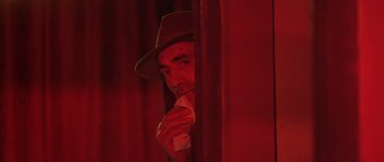 Movie still from “Malena” (2000), directed by Giuseppe Tornatore – A man in a hat is leaning against a red curtain; Close Up shot, Over the shoulder angle
