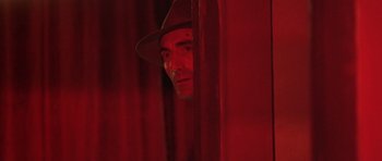 Movie still from “Malena” (2000), directed by Giuseppe Tornatore – A man in a hat looking through a red curtain; Close Up shot, Low angle