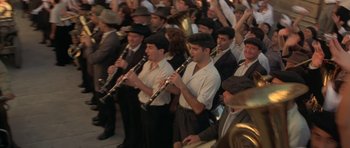 Movie still from “Malena” (2000), directed by Giuseppe Tornatore – A group of men in white shirts and black hats playing musical instruments; Wide shot, High angle