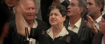 Movie still from “Malena” (2000), directed by Giuseppe Tornatore – An older woman is standing in front of a group of older men; Close Up shot, Low angle
