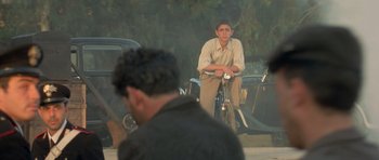 Movie still from “Malena” (2000), directed by Giuseppe Tornatore – A man sitting on top of a bicycle; Medium shot, Over the shoulder angle