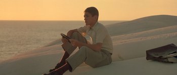 Movie still from “Malena” (2000), directed by Giuseppe Tornatore – A man sitting on the beach holding a steering wheel; Medium shot, Low angle