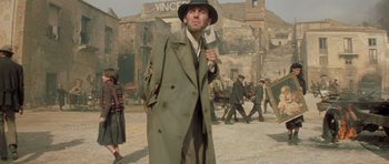 Movie still from “Malena” (2000), directed by Giuseppe Tornatore – A man in a trench coat and hat holding a knife; Medium shot, Low angle