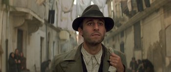 Movie still from “Malena” (2000), directed by Giuseppe Tornatore – A man in a hat and a jacket is standing in the street; Close Up shot, Low angle