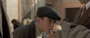 Movie still from “Malena” (2000), directed by Giuseppe Tornatore – A young man in a hat is smoking a cigarette; Close Up shot, Over the shoulder angle