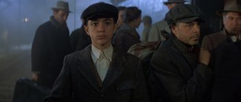 Movie still from “Malena” (2000), directed by Giuseppe Tornatore – A young man in a suit and a hat is standing in a crowd; Close Up shot, Low angle