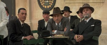 Movie still from “Malena” (2000), directed by Giuseppe Tornatore – A group of men sitting at a table with a tray of food; Medium shot, Over the shoulder angle