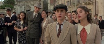 Movie still from “Malena” (2000), directed by Giuseppe Tornatore – A group of people standing in a line wearing suits and hats; Medium shot, Over the shoulder angle