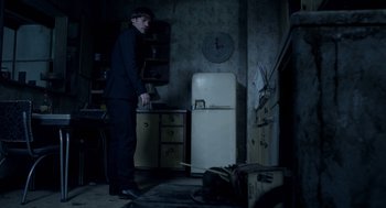 Movie still from “Mama” (2013), directed by Andy Muschietti – A man standing in a kitchen next to an old refrigerator; Wide shot, High angle