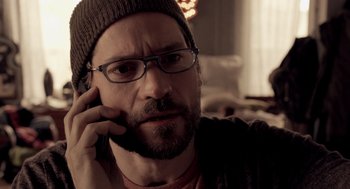 Movie still from “Mama” (2013), directed by Andy Muschietti – A man wearing glasses and a hat is talking on a cell phone; Close Up shot, Over the shoulder angle