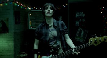 Movie still from “Mama” (2013), directed by Andy Muschietti – A person holding a guitar in a room with lights in the background; Medium shot, Low angle