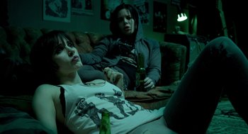 Movie still from “Mama” (2013), directed by Andy Muschietti – Two women sitting on a couch with a bottle of beer; Medium shot, High angle