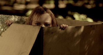 Movie still from “Mama” (2013), directed by Andy Muschietti – A little girl hiding behind a cardboard box; Close Up shot, High angle