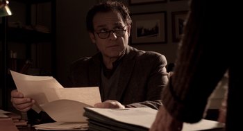 Movie still from “Mama” (2013), directed by Andy Muschietti – A man sitting at a table with papers in front of him; Medium shot, Over the shoulder angle