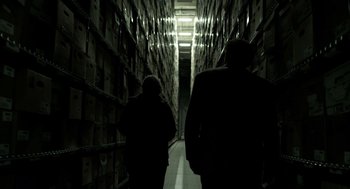 Movie still from “Mama” (2013), directed by Andy Muschietti – Two people are walking down a hallway in a warehouse; Wide shot, Low angle