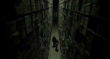 Movie still from “Mama” (2013), directed by Andy Muschietti – Two people are walking in a room full of boxes; Extreme Wide shot, Overhead angle