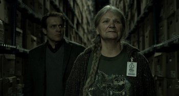 Movie still from “Mama” (2013), directed by Andy Muschietti – An older woman and a young man standing next to each other; Medium shot, Over the shoulder angle
