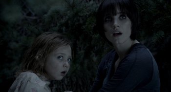 Movie still from “Mama” (2013), directed by Andy Muschietti – A woman and a child standing next to each other in front of trees; Close Up shot, Over the shoulder angle