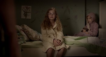 Movie still from “Mama” (2013), directed by Andy Muschietti – A young girl sitting on a bed wearing a robe; Medium shot, High angle