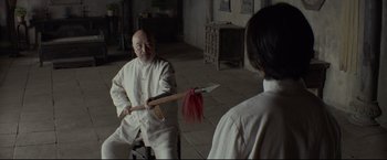 Movie still from “Man of Tai Chi” (2013), directed by Keanu Reeves – A man in a white robe is holding a red object; Medium shot, Over the shoulder angle