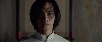 Movie still from “Man of Tai Chi” (2013), directed by Keanu Reeves – A man with long black hair wearing a white shirt; Close Up shot, Low angle