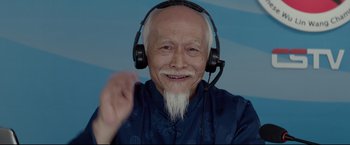 Movie still from “Man of Tai Chi” (2013), directed by Keanu Reeves – An older man with a beard and headphones on; Close Up shot, Low angle