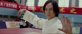 Movie still from “Man of Tai Chi” (2013), directed by Keanu Reeves – A man in a white shirt is holding his arm up; Close Up shot, Low angle