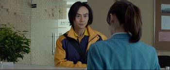 Movie still from “Man of Tai Chi” (2013), directed by Keanu Reeves – A man looking into a mirror while standing next to a woman; Medium shot, Over the shoulder angle