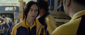 Movie still from “Man of Tai Chi” (2013), directed by Keanu Reeves – A man in a yellow and blue jacket is looking at the camera; Close Up shot, Over the shoulder angle