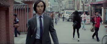 Movie still from “Man of Tai Chi” (2013), directed by Keanu Reeves – A man in a suit and tie walking down a street; Medium shot, Low angle