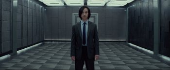 Movie still from “Man of Tai Chi” (2013), directed by Keanu Reeves – A man in a suit and tie standing in a room; Medium shot, Low angle
