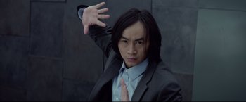Movie still from “Man of Tai Chi” (2013), directed by Keanu Reeves – A man in a suit and tie holding his hands up; Close Up shot, Low angle