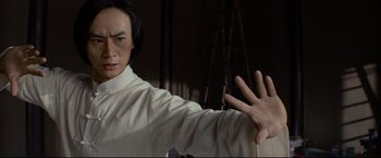 Movie still from “Man of Tai Chi” (2013), directed by Keanu Reeves – A man in a white shirt is holding his hands out; Medium shot, Low angle