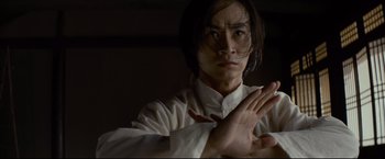 Movie still from “Man of Tai Chi” (2013), directed by Keanu Reeves – A man in a white shirt is practicing martial arts in a dark room; Close Up shot, Low angle