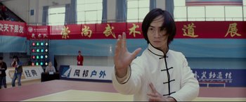 Movie still from “Man of Tai Chi” (2013), directed by Keanu Reeves – A man in a white shirt is practicing martial arts in a gym; Medium shot, Low angle