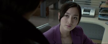 Movie still from “Man of Tai Chi” (2013), directed by Keanu Reeves – A woman in a purple jacket sitting in an office chair; Close Up shot, Over the shoulder angle