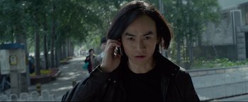 Movie still from “Man of Tai Chi” (2013), directed by Keanu Reeves – A man talking on a cell phone while walking down a street; Close Up shot, Low angle
