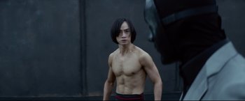 Movie still from “Man of Tai Chi” (2013), directed by Keanu Reeves – A man with long black hair is standing in front of a wall; Medium shot, Over the shoulder angle