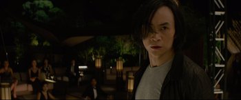 Movie still from “Man of Tai Chi” (2013), directed by Keanu Reeves – A young man standing in front of a group of people; Medium shot, Over the shoulder angle