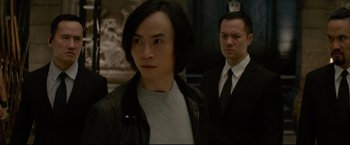 Movie still from “Man of Tai Chi” (2013), directed by Keanu Reeves – A man in a suit and tie standing next to another man in a suit and tie; Close Up shot, Over the shoulder angle