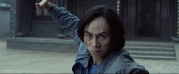 Movie still from “Man of Tai Chi” (2013), directed by Keanu Reeves – A man with long black hair is standing outside; Close Up shot, Low angle