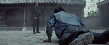 Movie still from “Man of Tai Chi” (2013), directed by Keanu Reeves – A man kneeling down in front of another man; Wide shot, Over the shoulder angle