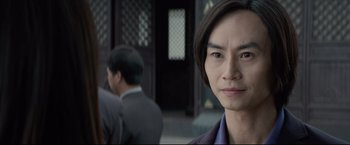 Movie still from “Man of Tai Chi” (2013), directed by Keanu Reeves – A man in a suit and tie standing in front of a building; Close Up shot, Over the shoulder angle