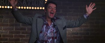 Movie still from “Man on the Moon” (1999), directed by Milos Forman – A man standing up with a microphone in front of a brick wall; Medium shot, Low angle