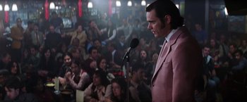 Movie still from “Man on the Moon” (1999), directed by Milos Forman – A man in a pink suit stands at a microphone in front of a crowd; Medium shot, Over the shoulder angle