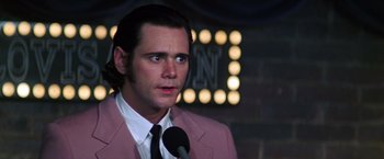 Movie still from “Man on the Moon” (1999), directed by Milos Forman – A man in a pink jacket is speaking into a microphone; Close Up shot, Low angle