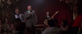 Movie still from “Man on the Moon” (1999), directed by Milos Forman – A man in a suit and tie singing into a microphone; Medium shot, Over the shoulder angle